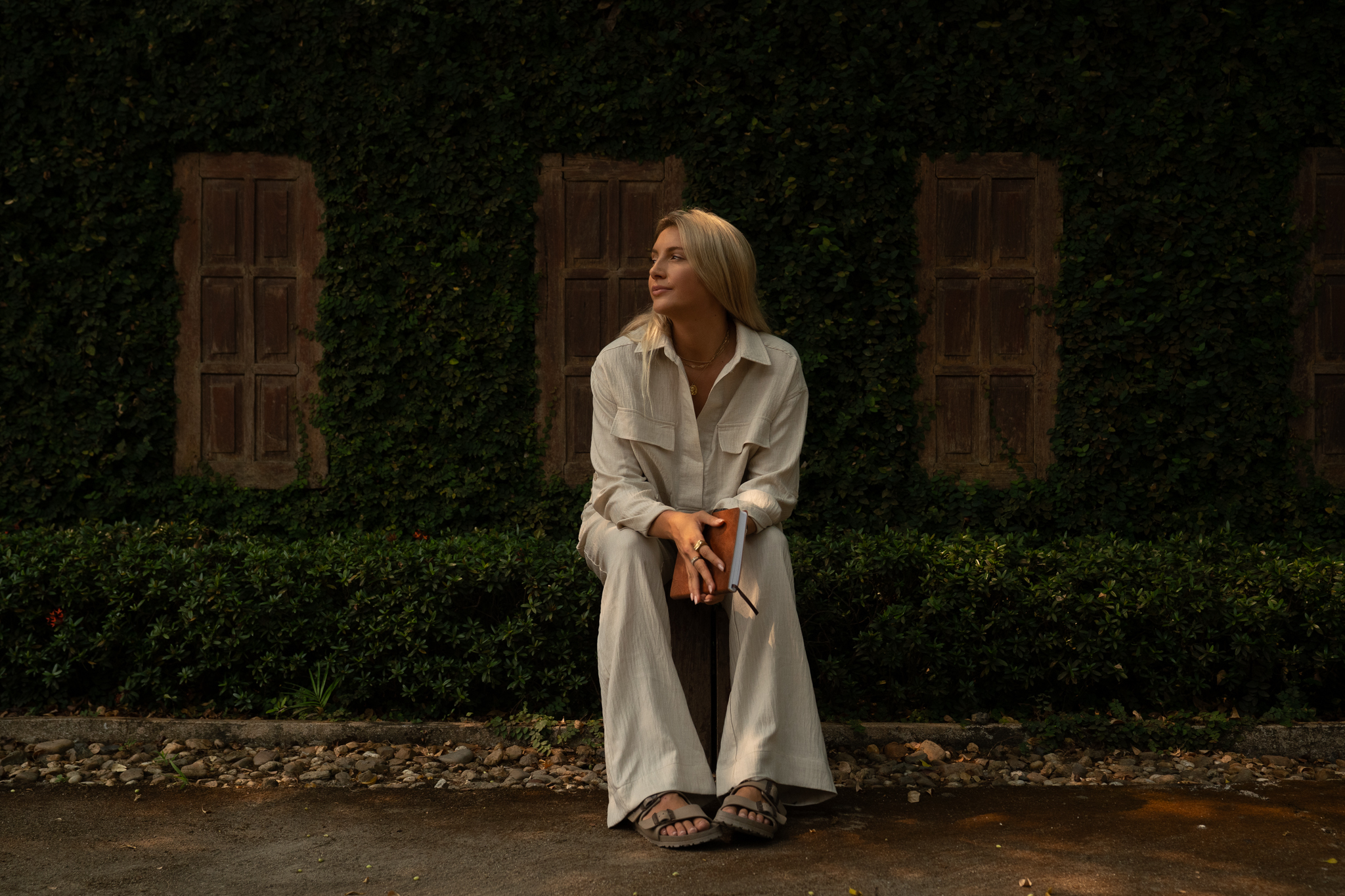 Anna Bucklar seated in front of an ivy-covered wall in soft evening light, holding a leather journal